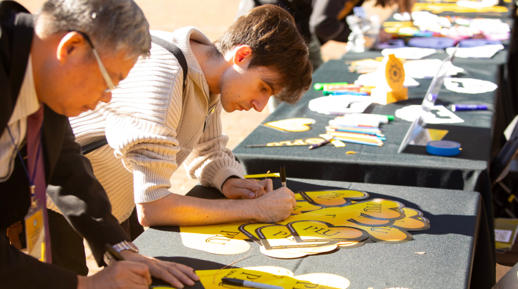 Two people lean over a table signing yellow paper hearts.