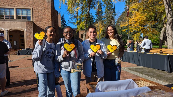Four students smile into the camera holding yellow paper hearts.