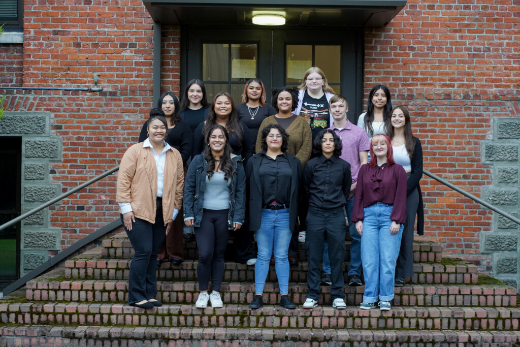 A group of students stand on stairs outside and look into the camera and smile.