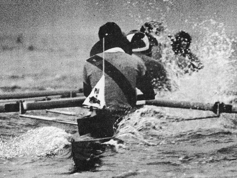 A black and white photograph of the PLU rowing team rowing a boat to PLU.