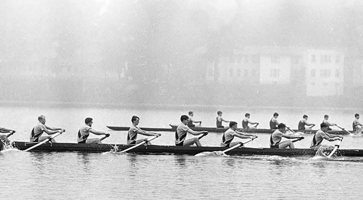 A black and white photograph of two boats competing in a rowing competition on a lake.