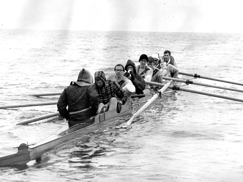 A black and white photo of the PLU rowing team in a row boat on the water.