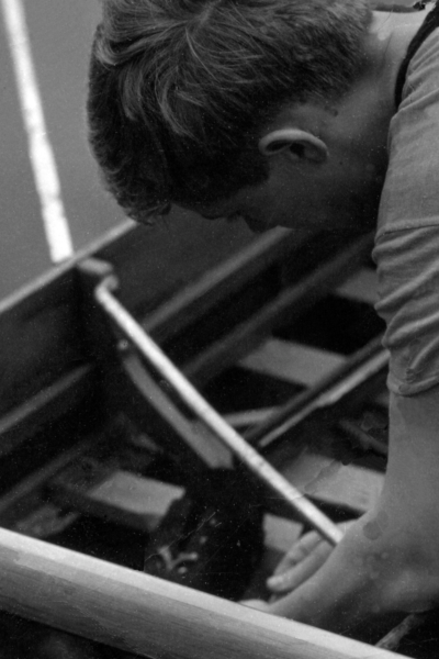 A black and white photograph of a boy fixing a row boat, close up.