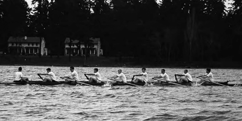 A black and white photograph of rowers rowing on a lake.