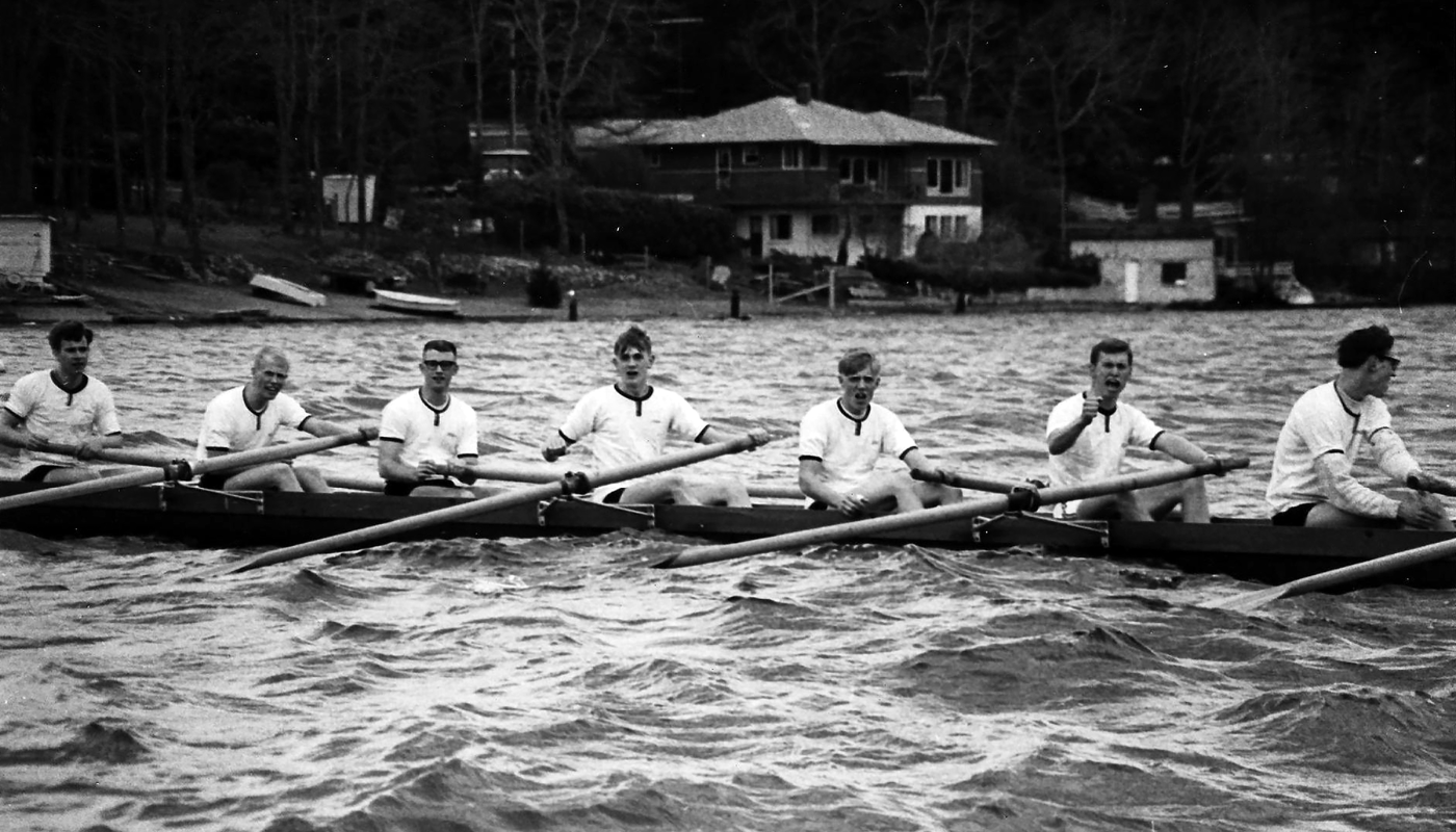 A black and white photograph of rowers in a boat on a lake.