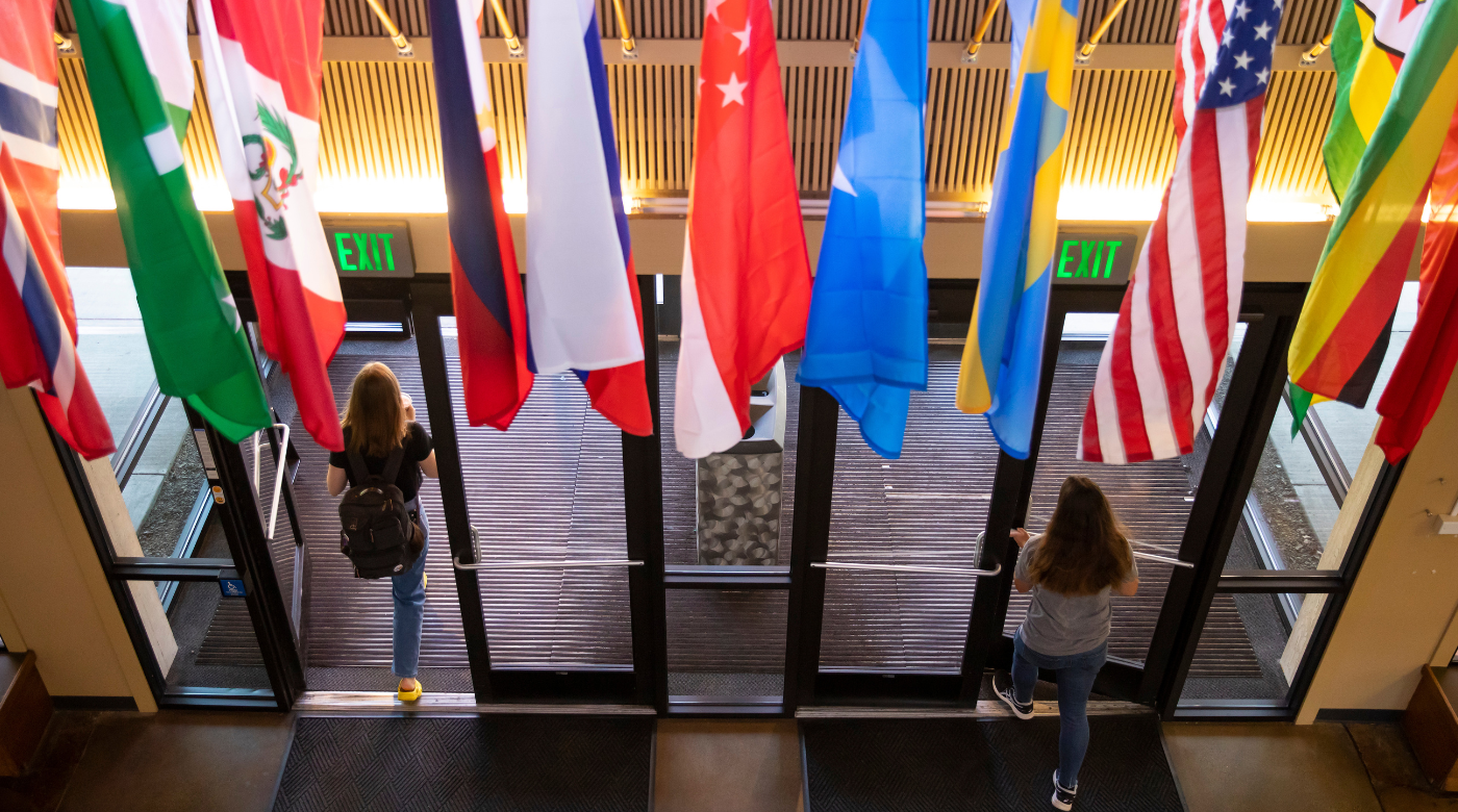 Two students walk through doors. Flags of different countries hang down over the doors.