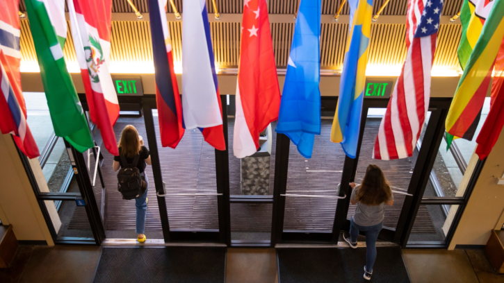 Two students walk through doors. Flags of different countries hang down over the doors.