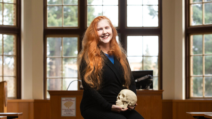 Brenda Llewellyn Ihssen sitting in the large lecture hall in PLU's Xavier Hall. She is smiling, wearing black, and holding a model skull in her hands.
