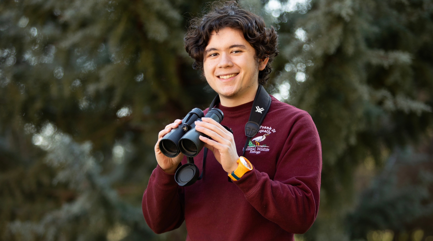 PLU senior Elijah Paez looks into the camera and smiles while holding binoculars.