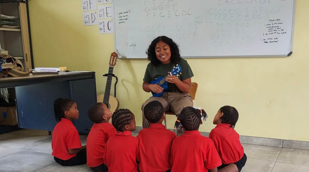 Jessa playing ukulele for Namibian students who are sitting around her.
