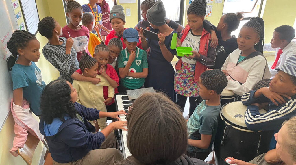 Jessa sitting at a keyboard while Namibian students stand around her.