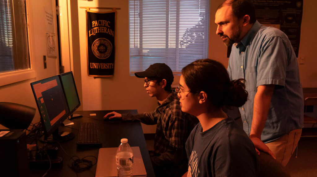 A plu professor and two students all look together at a computer in the astronomy lab.