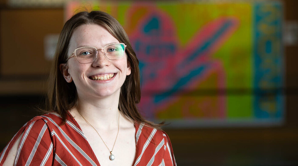 Lindsey Clark smiling into the camera in front of a brightly colored piece of wall art behind her.