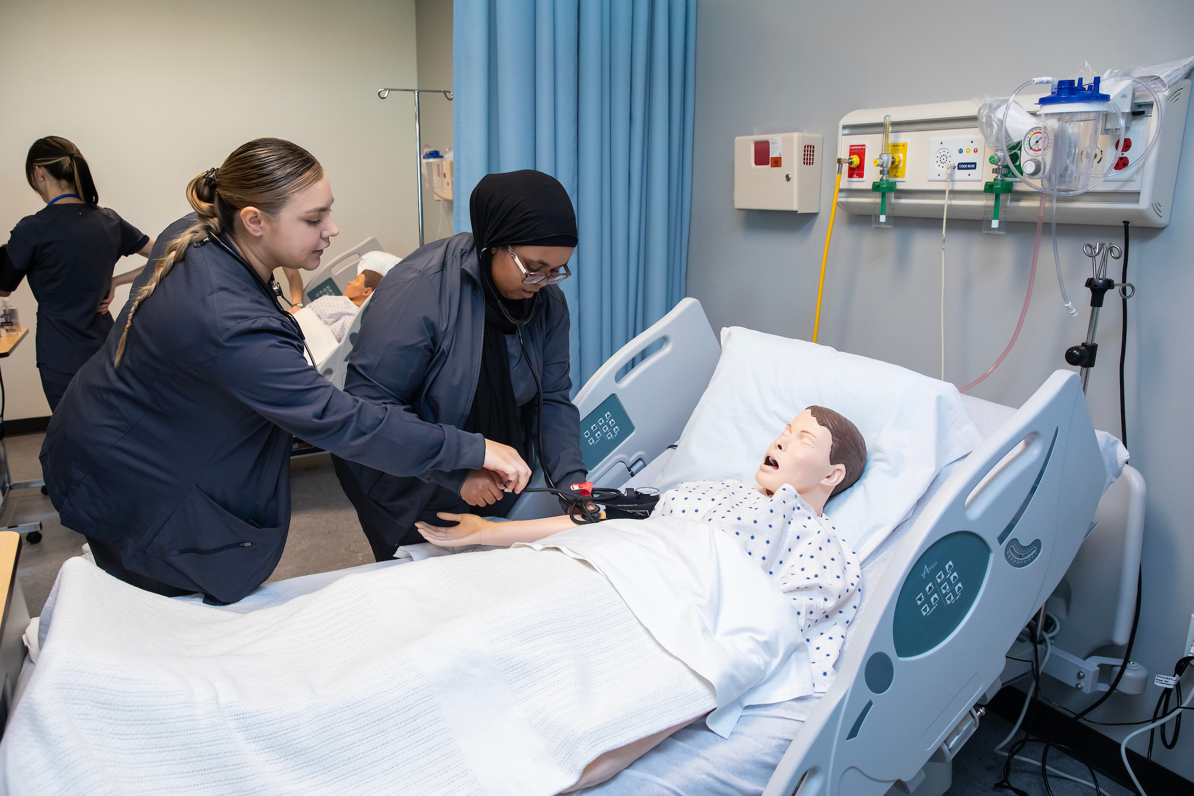 two students look over a dummy as they take it's pulse