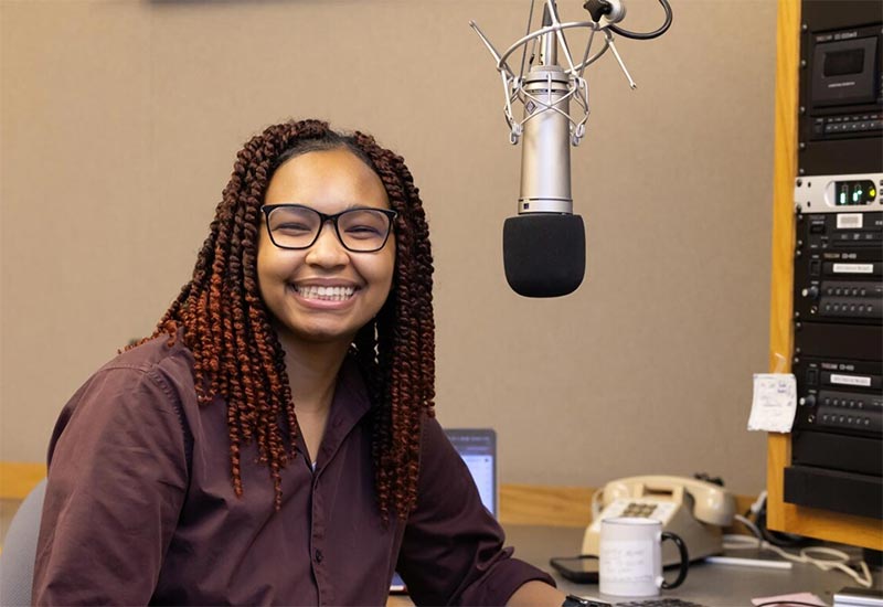 Zari Warden smiling and sitting next to a microphone in a recording booth.