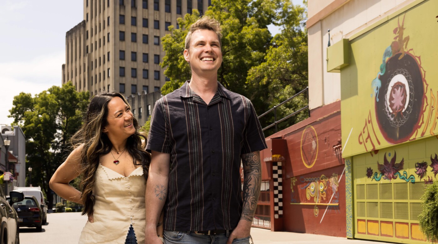 Chris Staudinger ’08 and Tawny Clark ’08, founders of Pretty Gritty Tours, hold hands and smile in downtown Tacoma on a sunny day.