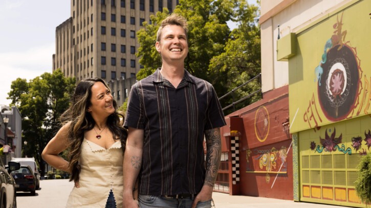 Chris Staudinger ’08 and Tawny Clark ’08, founders of Pretty Gritty Tours, hold hands and smile in downtown Tacoma on a sunny day.