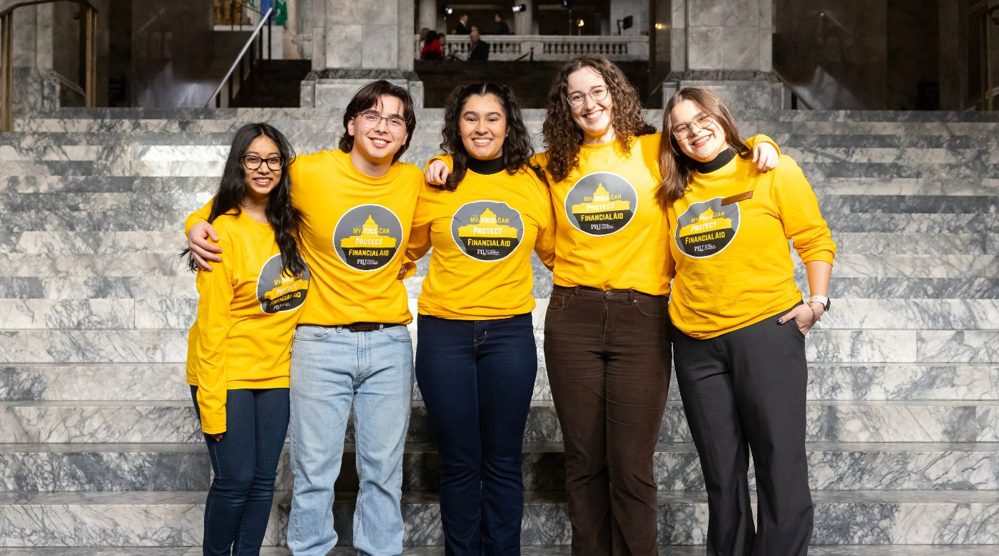 Five PLU students stand on the steps of the Washington State Capitol while wearing yellow shirts that say "My voice can protect financial aid."