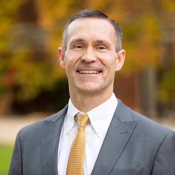 David Ward smiles in a gray suit coat, white shirt, and yellow tie.