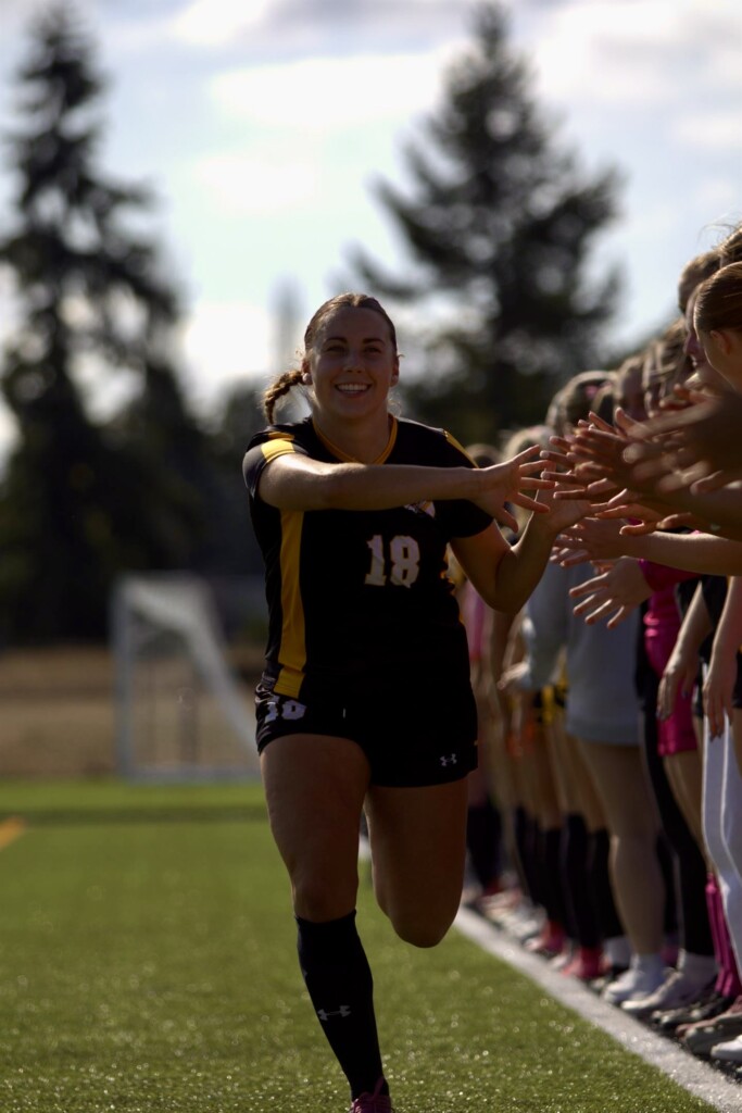 Smiling student Carmen Kiewert runs across the the soccer field and gives high fives to her teammates.