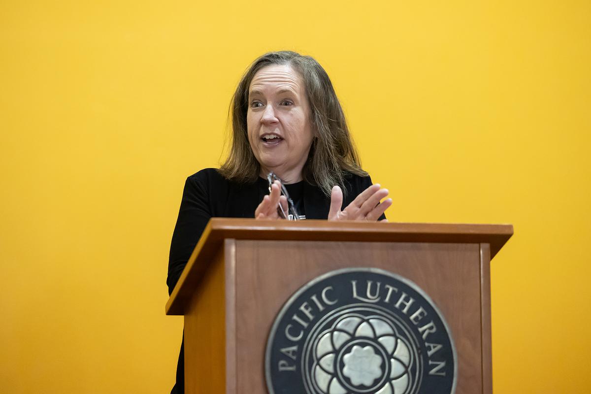 A woman speaking at a podium with a Pacific Lutheran logo.