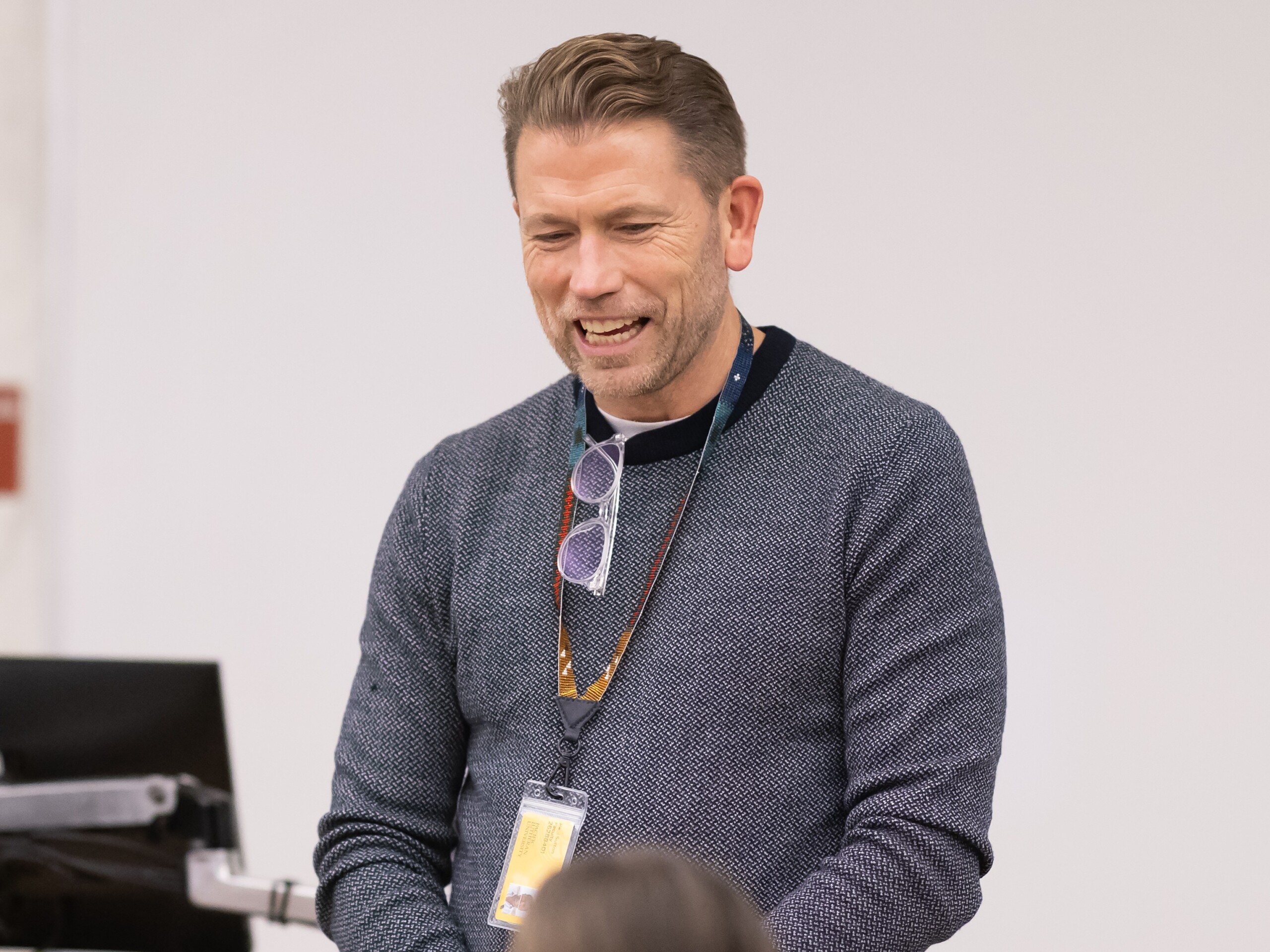 Professor Paul Sutton is laughing in a blue sweater and his PLU ID and glasses hanging from the neckline of his shirt.
