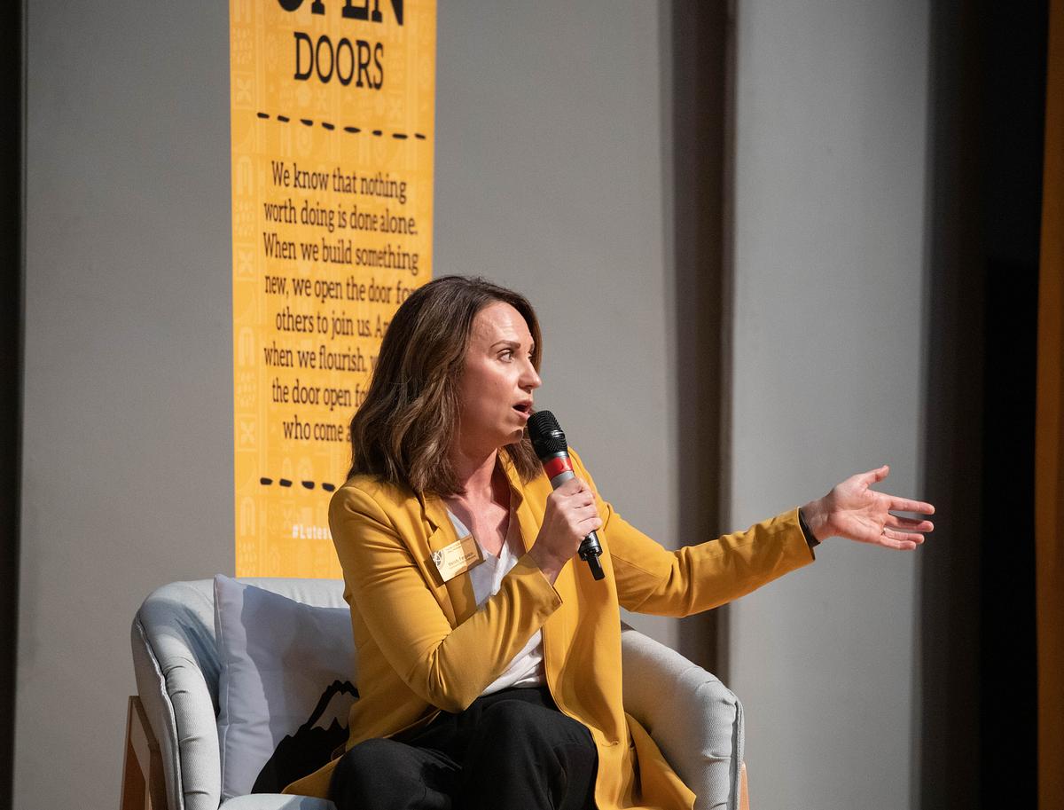 Woman in yellow jacket speaking on stage.