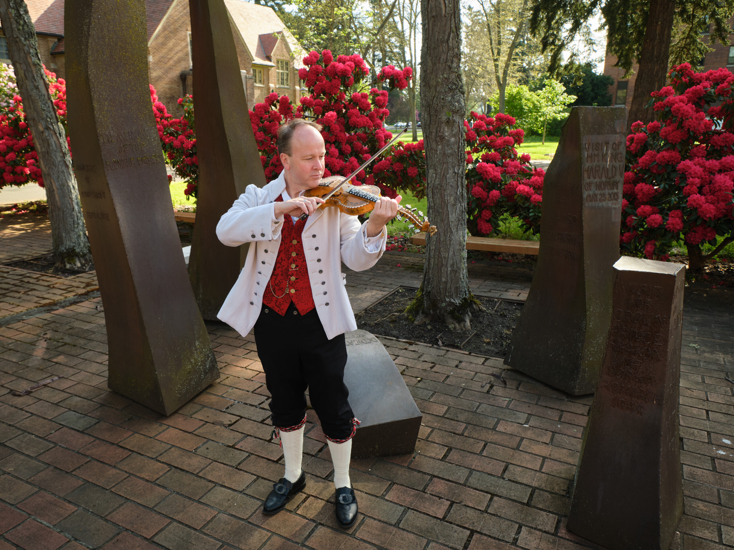 A man in colonial attire playing a fiddle outdoors.