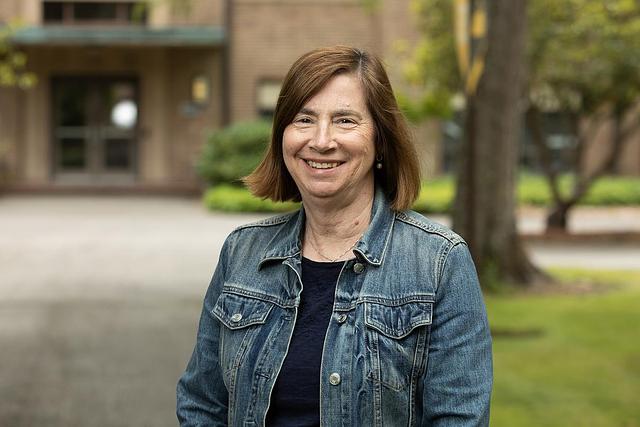 Jan Weiss smiles in denim jacket outdoors on campus.