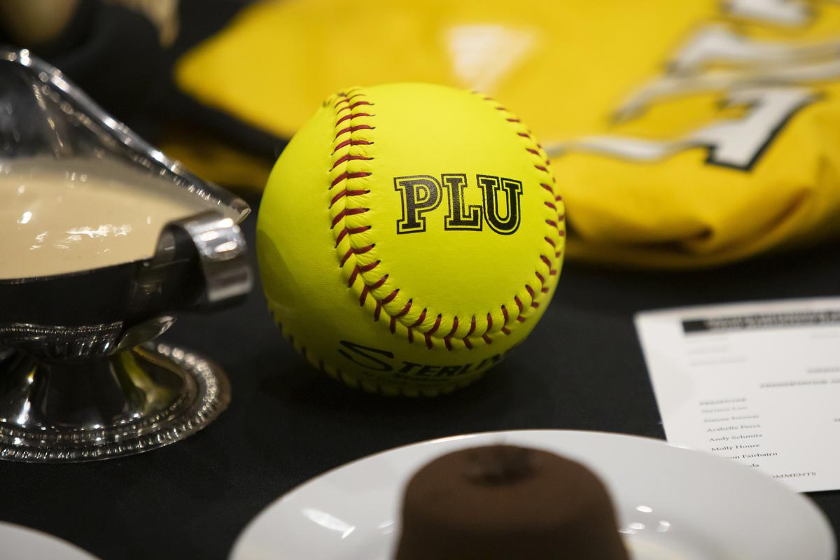 Yellow softball with "PLU" text on a sports background.