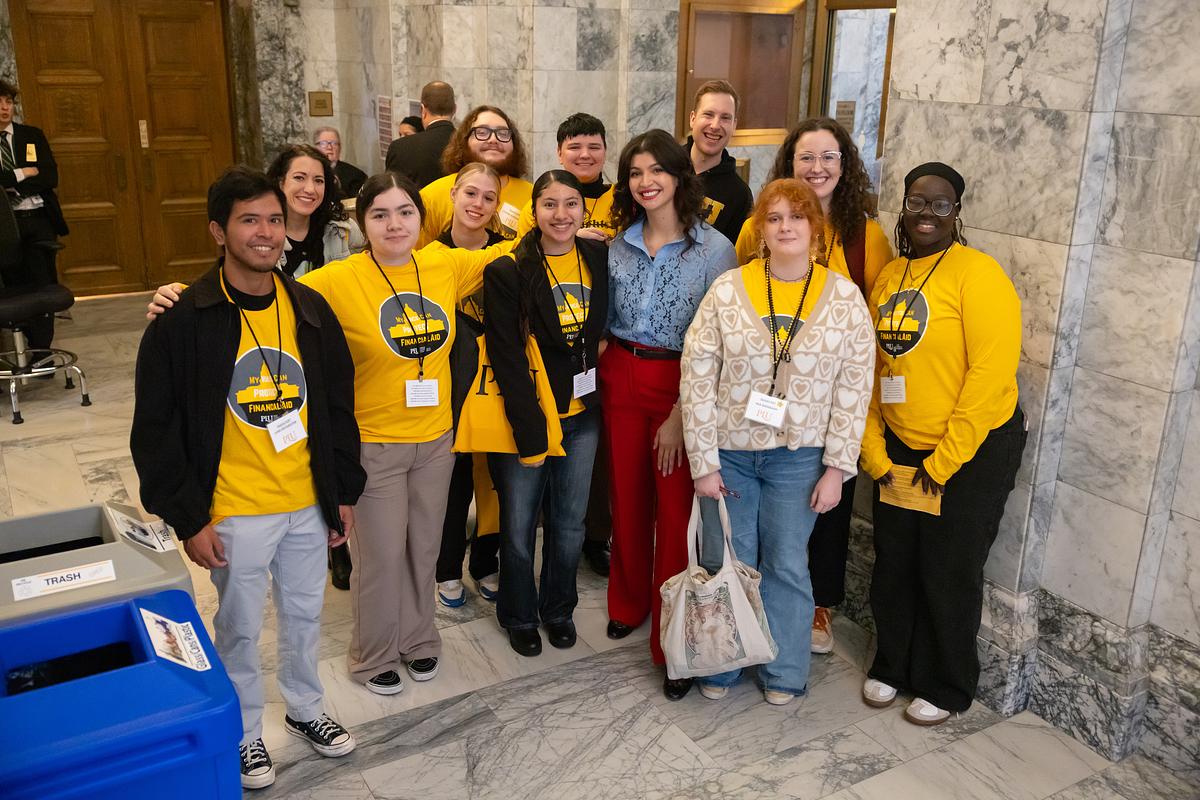 A group of PLU students in yellow shirts take a photo with Washington State Representative Sharlett Mena.