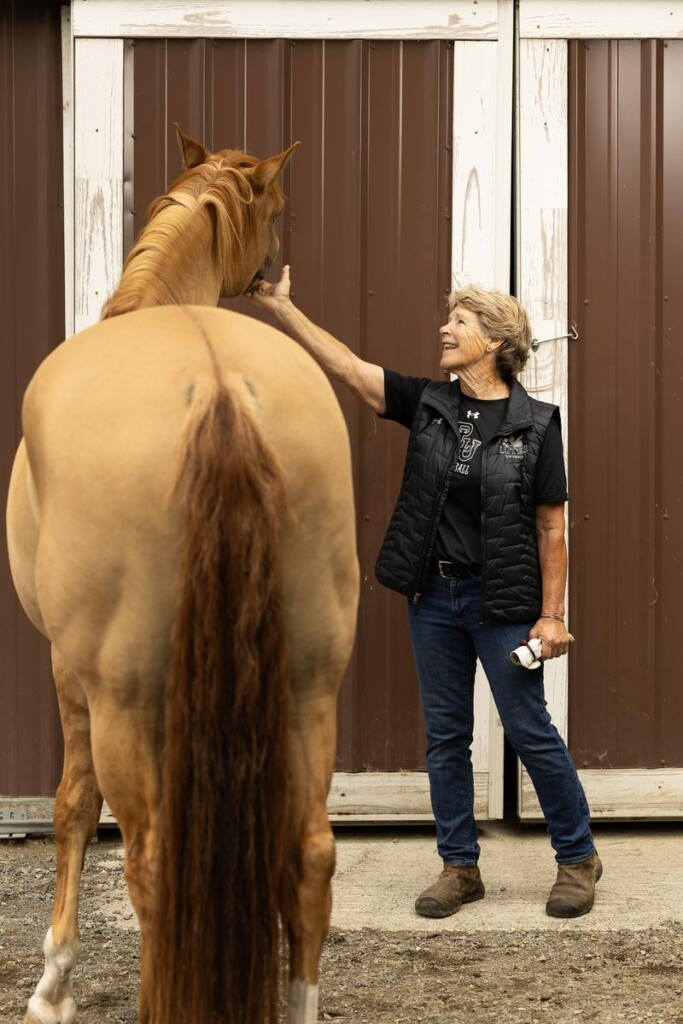 20260717_SB_Cindy-Resolute-Softball_022-medium Cindy Van Hulle, wearing leather boots, blue jeans, and a black sweater, laughs as she pets a horse.