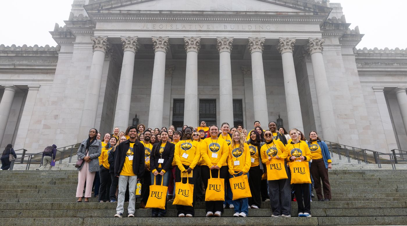 Over 50 PLU students in yellow shirts that read "My voice can protect financial aid," smile for a group photo in front of the Washington State Capitol in Olympia, WA. (PLU Photo / Sy Bean)