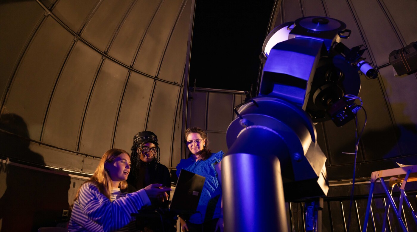 Four people using telescope in illuminated observatory dome