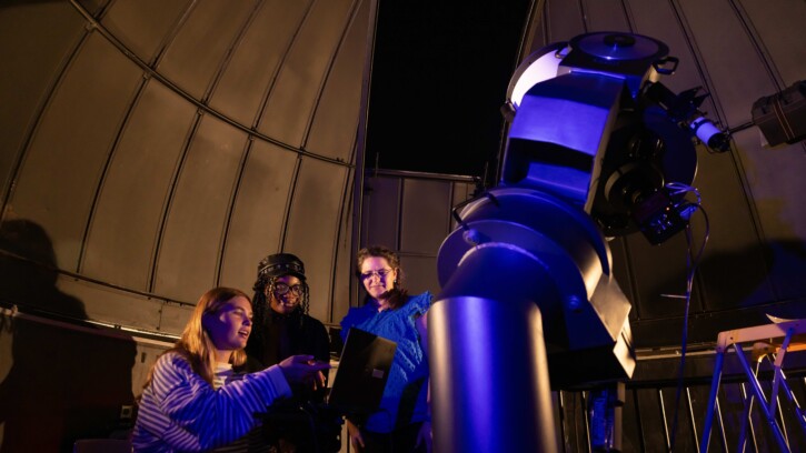 Four people using telescope in illuminated observatory dome