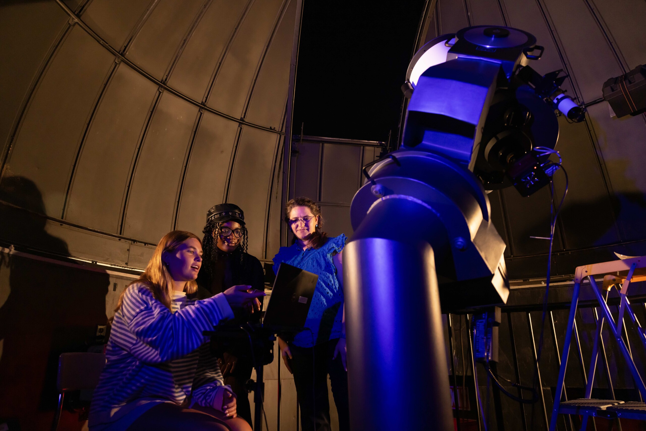 Four people using telescope in illuminated observatory dome