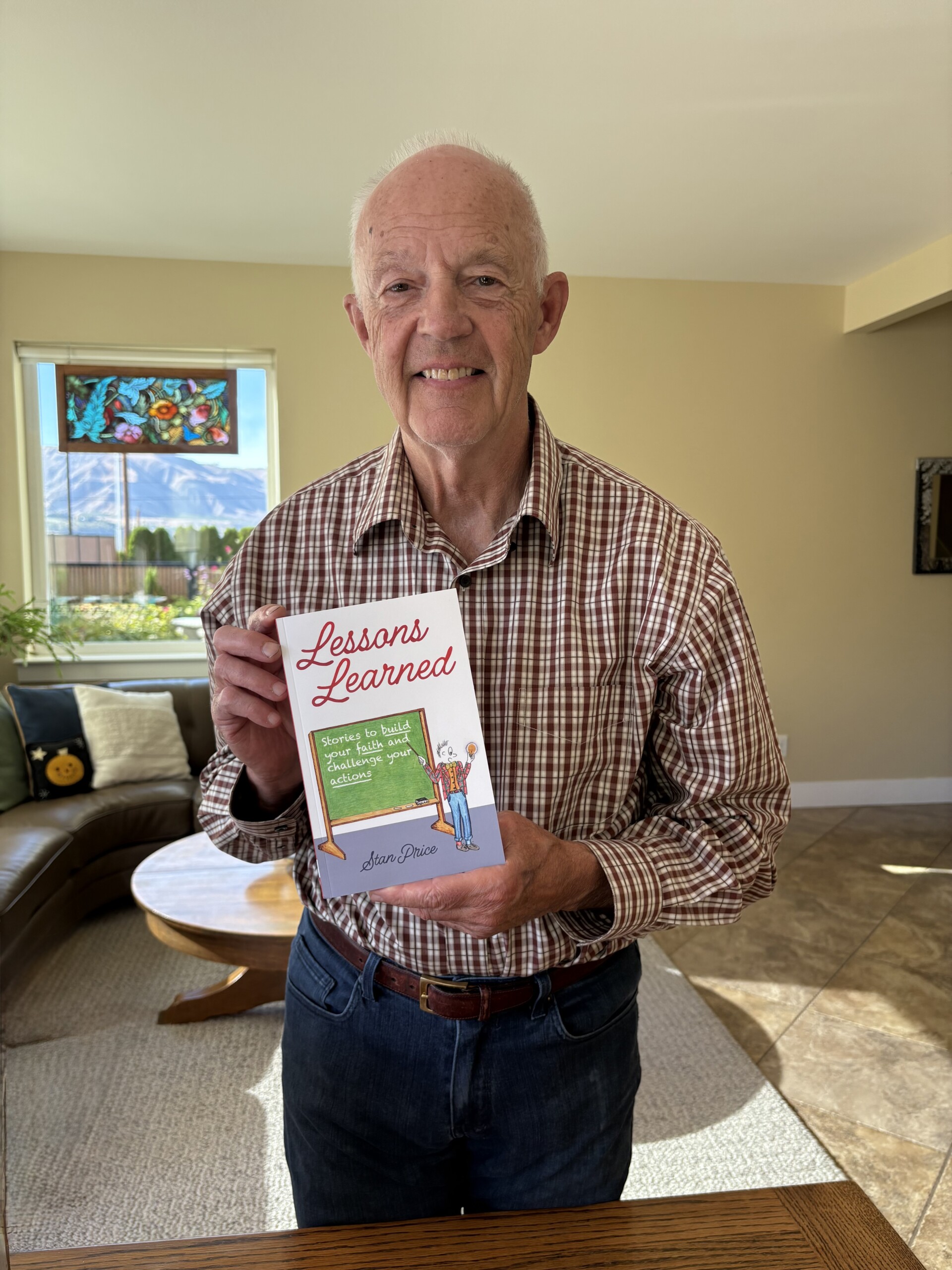 Stan Price smiles in a livingroom while holding his book, "Lessons Learned: Stories to Build Your Faith and Challenge Your Actions."