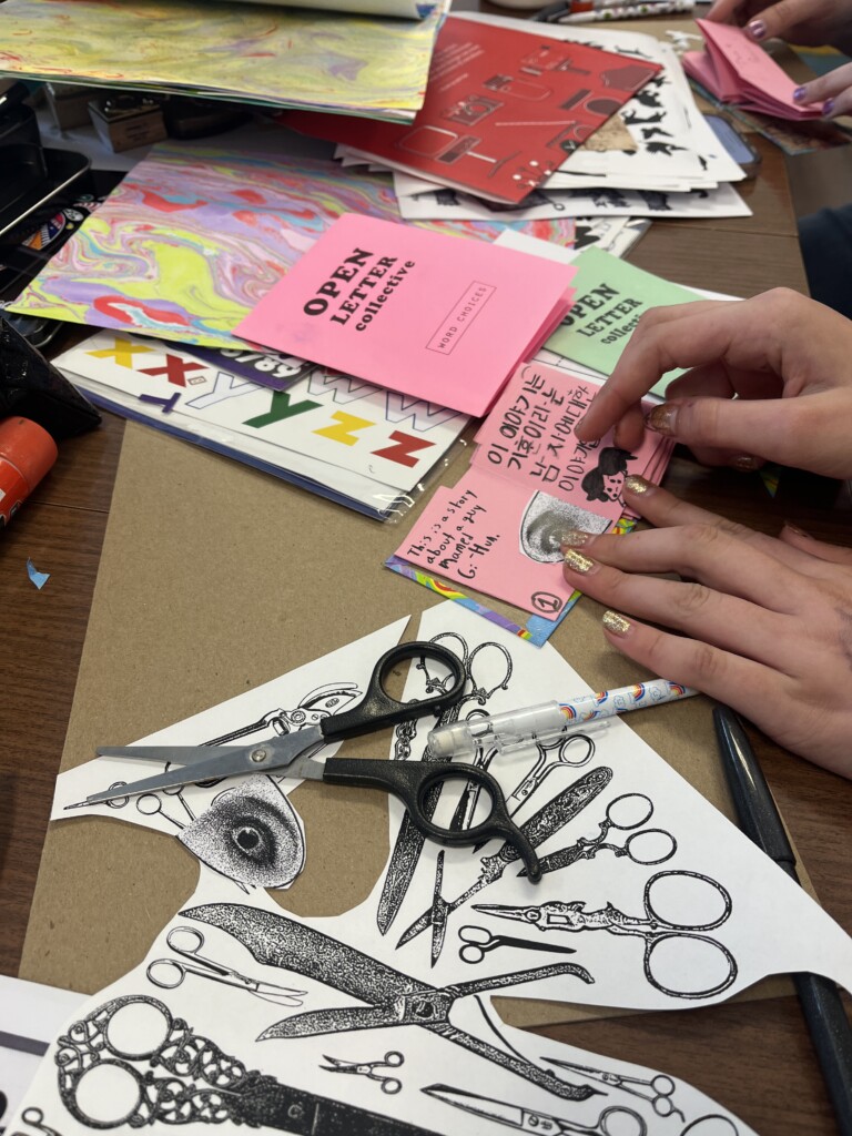 Hands working on small zines on an art work surface.