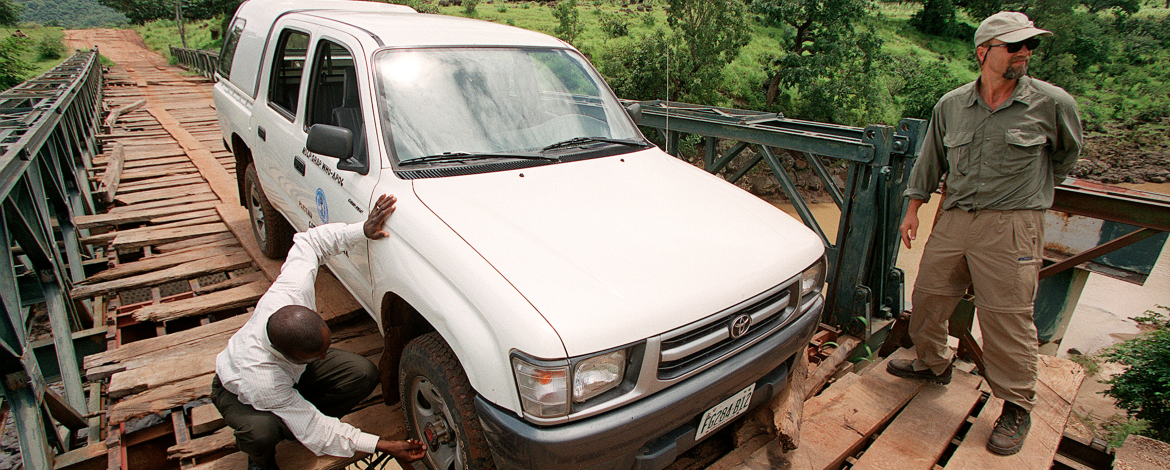 Tom on a bridge with a man repairing a jeep tire.