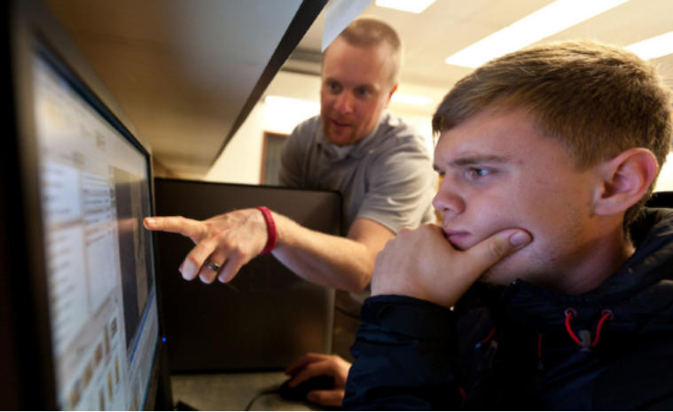 Student looking at computer monitor while a teacher points at the screen