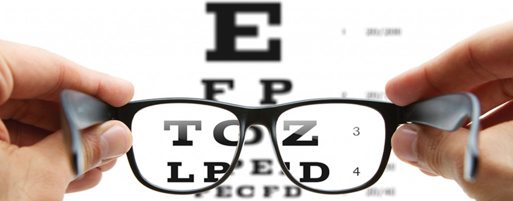pre-optometry up close photo of hands holding glasses in front of eye chart