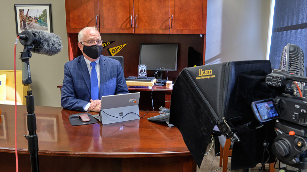 Belton masked at his desk addressing the PLU community on camera