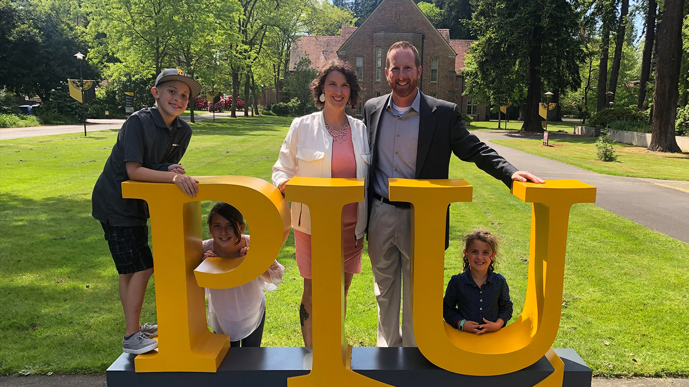 PLU athletic director Mike Snyder and his wife and three kids pose by the PLU sign on a sunny day.