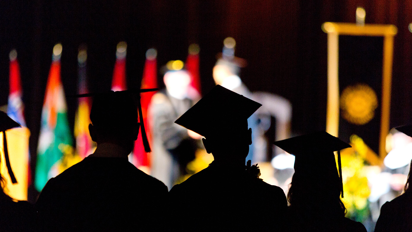 photograph taken behind three PLU students at commencement as they look up on stage