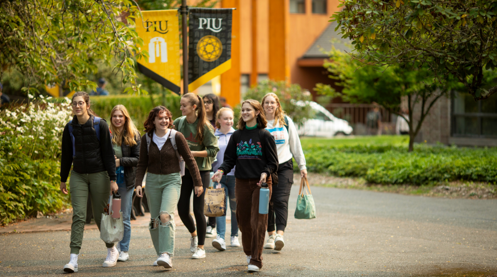 Students walk on campus in a group. There are PLU banners in the background.