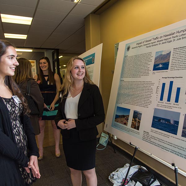 Two PLU students look at a big posterboard