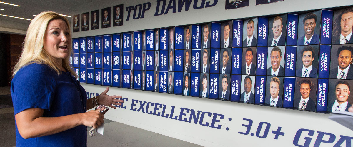 Jen Cohen standing in front of the "Top Dawgs 3.0 GPA" wall at UW