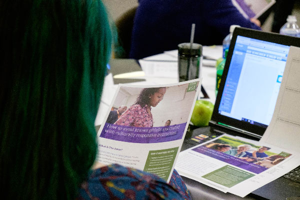 A women is looking at a piece of paper with a computer on a table