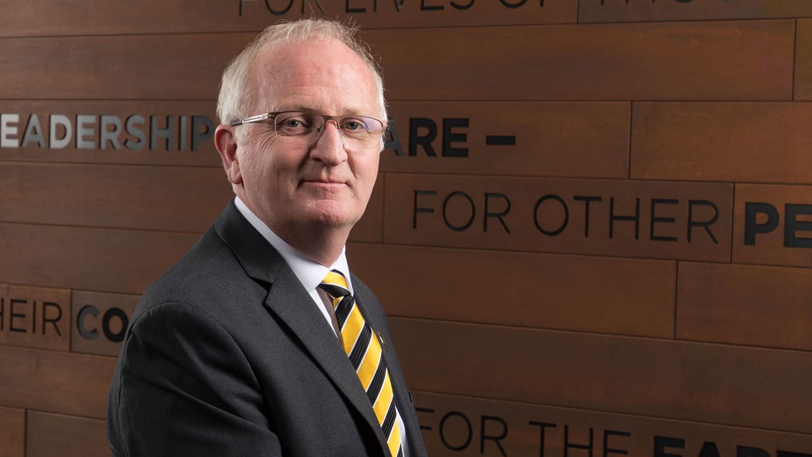 PLU President, Allan Belton, standing in an office with words on the wall behind him