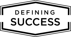 A badge logo that reads Defining Success